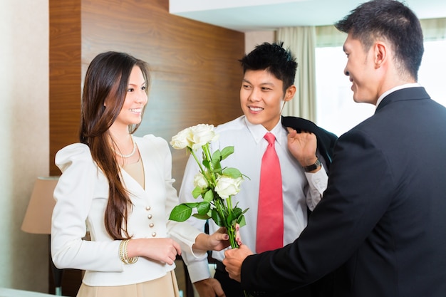 El gerente, director o supervisor del hotel chino asiático da la bienvenida a los huéspedes VIP que llegan con rosas a su llegada al hotel de lujo o gran