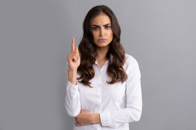 Gerente ejecutivo de mujer fruncir el ceño mantener el dedo apuntando hacia arriba fondo gris, idea.