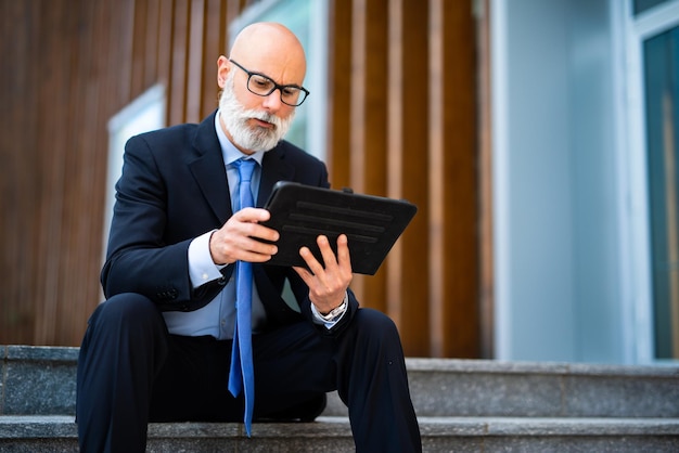 Gerente elegante usando seu tablet sentado em um banco ao ar livre em uma cidade moderna