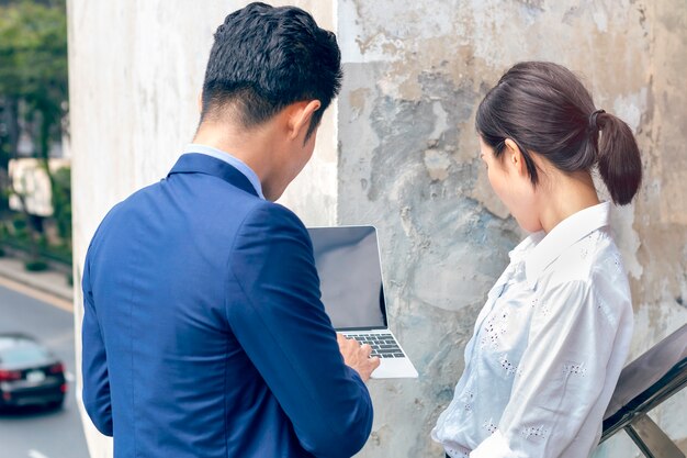 Foto gerente empresarios asiáticos discutiendo ideas con laptop reunión mujer de negocios fuera. vista posterior.