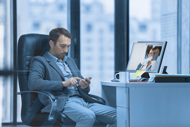 El gerente está hablando por teléfono, junto a la computadora, que tiene noticias sobre el coronavirus.