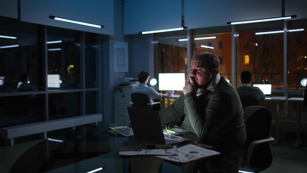 Gerente estressado com excesso de peso trabalha até tarde no laptop no escritório