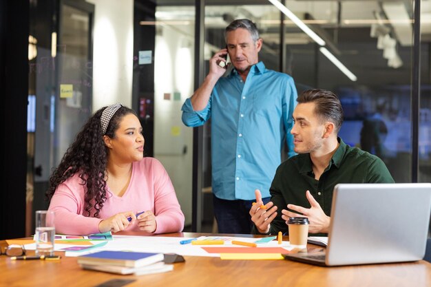 Foto gerente falando no telefone inteligente olhando para colegas multirraciais discutindo estratégia no escritório