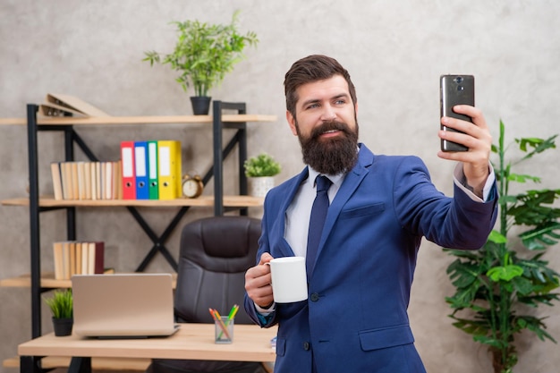 Gerente feliz sonriendo al teléfono inteligente en la oficina selfie