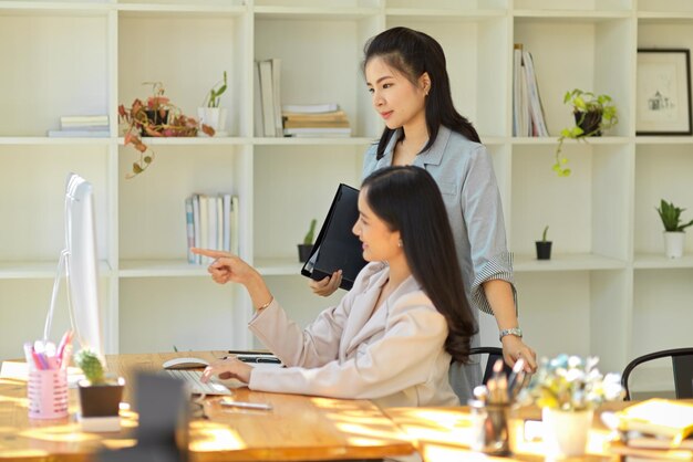 Gerente femenina informando y revisando el trabajo de sus asistentes en la pantalla de escritorio de la PC en la oficina