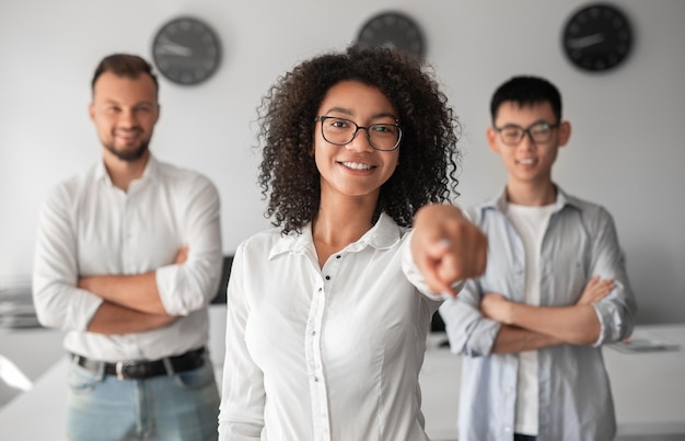 Foto gerente feminina afro-americana apontando para a câmera perto de colegas de trabalho no escritório