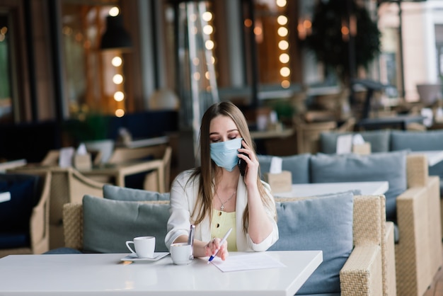 Gerente feminina de terno e máscara médica trabalha remotamente em um café de rua