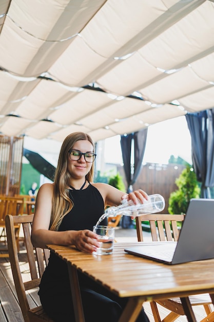 Gerente feminina freelancer aproveitando a pausa para o café no terraço de verão de um café aconchegante trabalhando remotamente no laptop sorrindo olhando para o laptop Trabalho on-line no verão