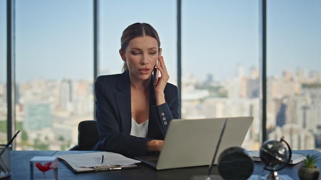 Gerente financiero hablando con teléfono inteligente en el escritorio joven mujer de negocios trabajando con computadora portátil