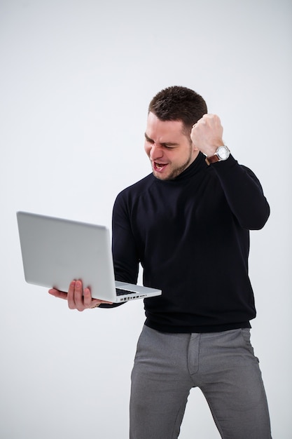 Un gerente hombre de negocios sonríe y se para con una computadora portátil en sus manos y mira la pantalla. Se coloca sobre un fondo blanco.
