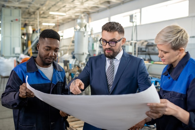 Gerente industrial com tablet conversando com um trabalhador e examinando peças de metal produzidas na loja da fábrica