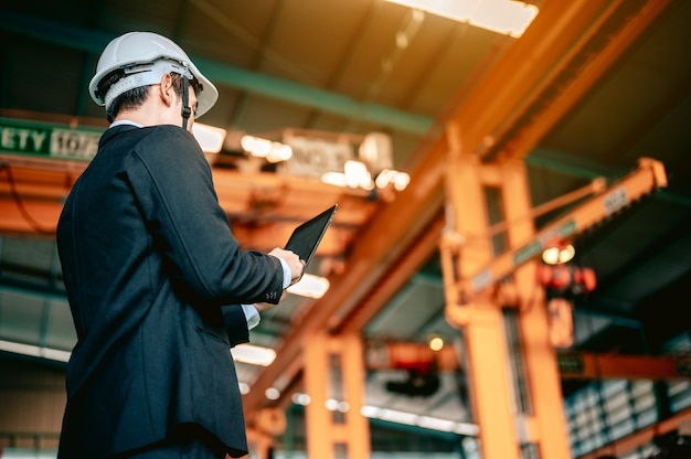 El gerente del ingeniero revisa el manual en la tableta y ordena al trabajador que use la mano del robot de la máquina del torno