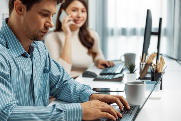 Gerente inteligente escribiendo en la computadora portátil mientras la compañera de trabajo llama por teléfono Postulado