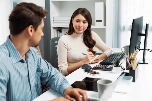 Gerente inteligente hablando con una compañera de trabajo mientras escribe en la computadora portátil Postulado