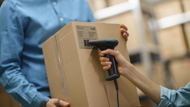 Gerente de inventario femenina escanea una caja de cartón y con un escáner de códigos de barras Trabajador masculino sostiene un paquete en las filas de fondo de cajas de cartón con productos listos para el envío