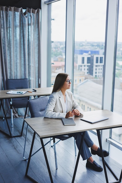 Gerente jovem bem sucedida em uma jaqueta casual elegante e óculos ópticos senta-se no escritório no local de trabalho uma mulher experiente com um laptop moderno trabalhando no escritório