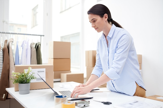 Gerente joven serio que se concentra en el trabajo sobre los pedidos en línea de los clientes mientras mira la pantalla del portátil