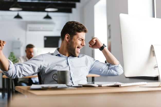 Foto gerente masculino alegre se regocija mientras usa la computación