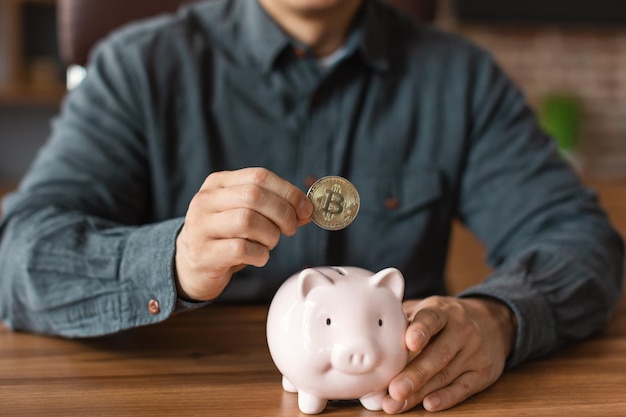 Gerente masculino asiático maduro coloca moeda bitcoin no cofrinho no interior do escritório doméstico recortado de perto