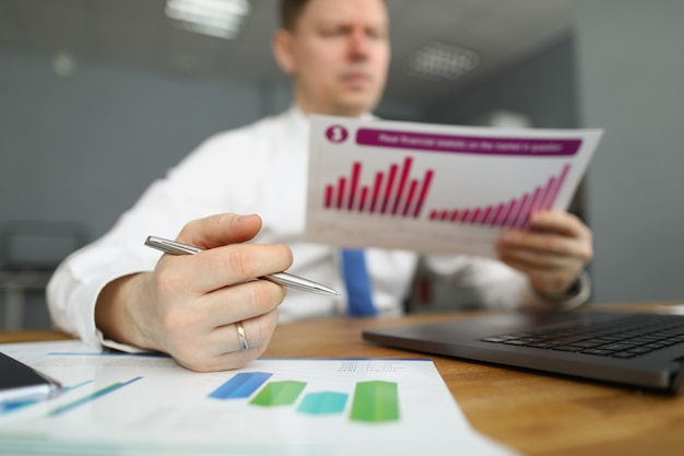 Un gerente masculino con una camisa se sienta en una mesa y sostiene un informe financiero con un diagrama