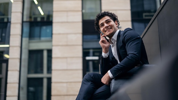 Un gerente masculino con traje oficial sostiene un teléfono en sus manos y llama a un colega de trabajo