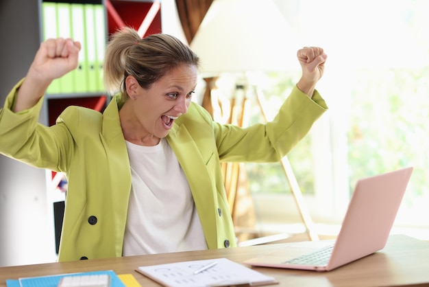 Gerente mujer feliz mirando la pantalla de la computadora mientras está sentado en el escritorio