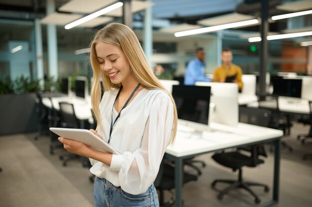 Gerente mujer sonriente sostiene portátil, interior de la oficina de TI en el fondo. Trabajador profesional, planificación o lluvia de ideas. Empleado exitoso en empresa moderna