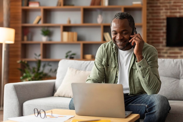 Gerente negro de meia-idade sorridente digitando no computador ligando por telefone para falar com o cliente