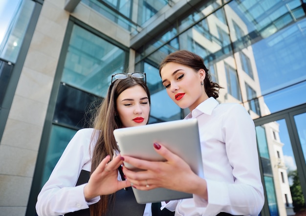 Gerente novo de duas mulheres de negócio na roupa clássica do escritório que olha a tabuleta e a fala do computador.