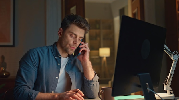 Gerente ocupado hablando teléfono inteligente noche PC lugar de trabajo primer plano hombre mirando monitor