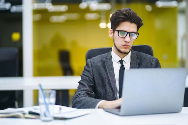 Gerente de oficina joven que trabaja con papeles y computadora en la oficina. El empresario escribe, revisa y analiza documentos.