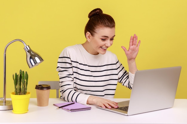 Gerente de oficina de mujer amigable saludando la mano a la pantalla del portátil hablando en videollamada con un amigo