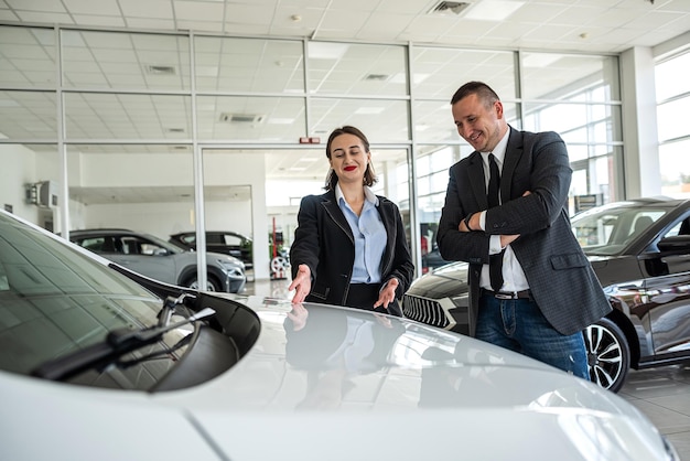 Foto gerente profissional mostra e leva carro para cliente feminina na concessionária