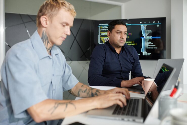 Foto gerente de proyecto serio trabajando en una computadora portátil mientras está sentado al lado del desarrollador