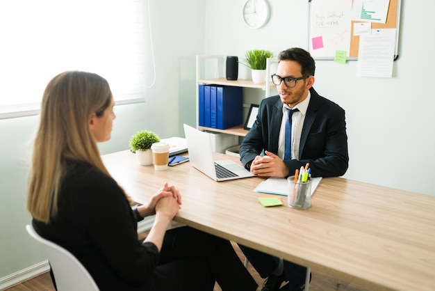 Gerente de recursos humanos hispano con traje y hablando con una candidata para un nuevo trabajo durante una entrevista en una oficina corporativa de negocios