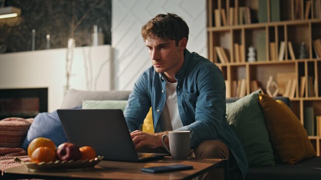 Gerente remoto digitando laptop sentado na sala de estar em close-up homem se sentindo sobrecarregado de trabalho