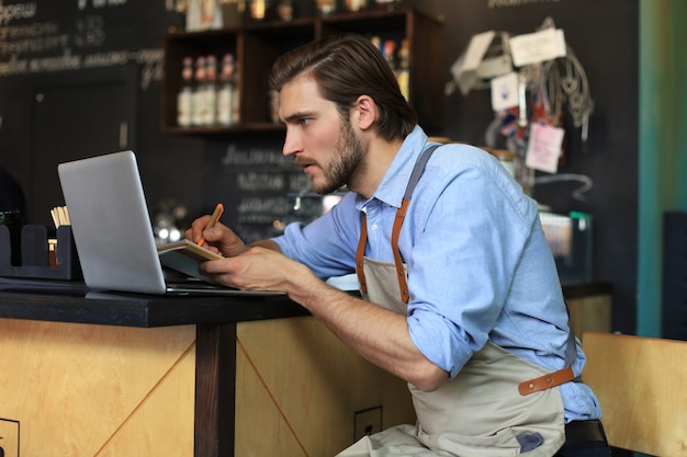 Gerente de restaurante que trabaja en la computadora portátil, contando los beneficios.