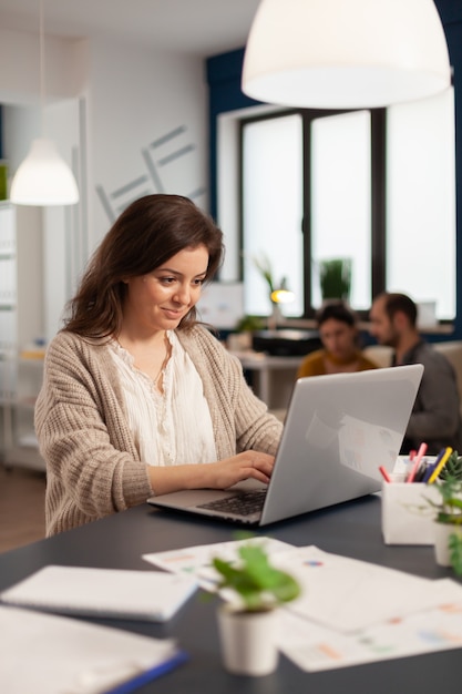 Foto gerente satisfeito, verificando estatísticas financeiras e gráficos, digitando no laptop sentado na mesa, trabalhando em uma empresa iniciante