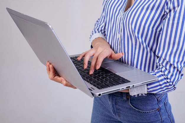 Gerente de sexo femenino en una camisa rayada blanco-azul con una computadora portátil que se coloca en gris. Empleada del año, mujer de negocios. Trabajador.