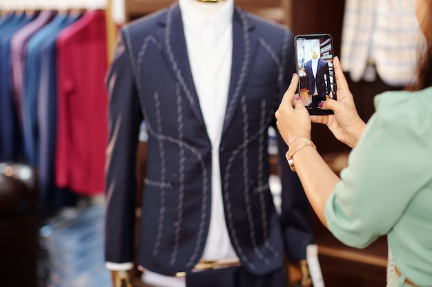 Gerente de taller femenino fotografiando chaqueta a medida casi lista en maniquí