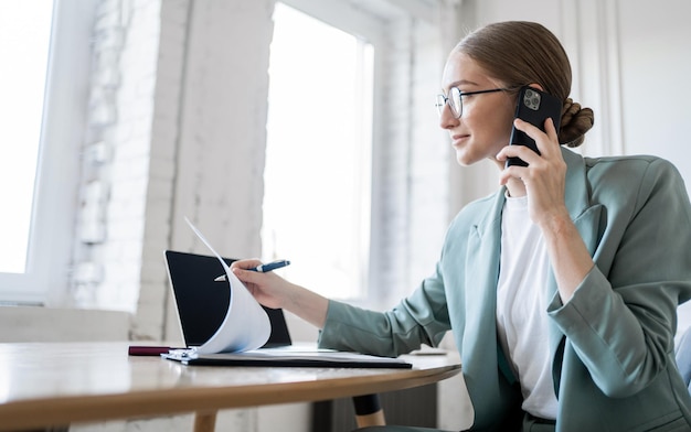 Una gerente usa una computadora portátil para contestar el teléfono de un cliente en la oficina