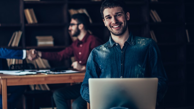 Gerente de ventas creativo con portátil en el fondo del apretón de manos de socios comerciales en una oficina moderna