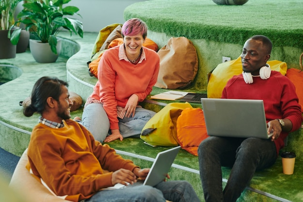 Gerentes interculturales jóvenes felices de una gran oficina contemporánea de espacios abiertos intercambiando ideas y discutiendo nuevas ideas en la reunión de puesta en marcha