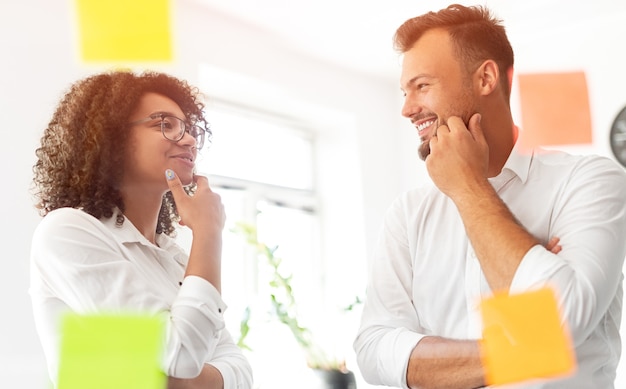 Gerentes multiétnicos sonriendo y mirándose mientras discuten el problema durante el trabajo en el proyecto durante el trabajo en el espacio de trabajo contemporáneo juntos