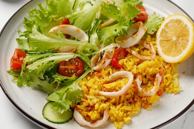 Gericht mit Tintenfischringen Reis grüner Gemüsesalat mit Tomatengurken auf weißem Teller Nahaufnahme