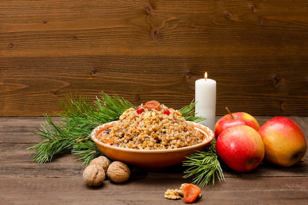 Gericht mit traditioneller slawischer Leckerei an Heiligabend auf braunem Holzbrett Kiefernzweige Äpfel Walnüsse Kerze Kopierraum