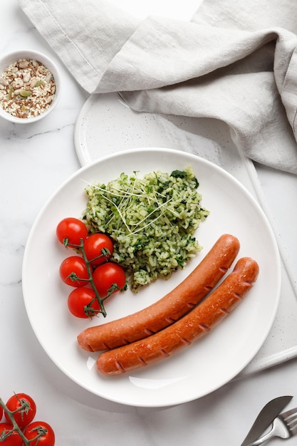 Gericht mit Würstchen und Reis mit Spinat und Microgreens auf weißem Teller Gebratene leckere Würste Keto-Diät-Essen Draufsicht