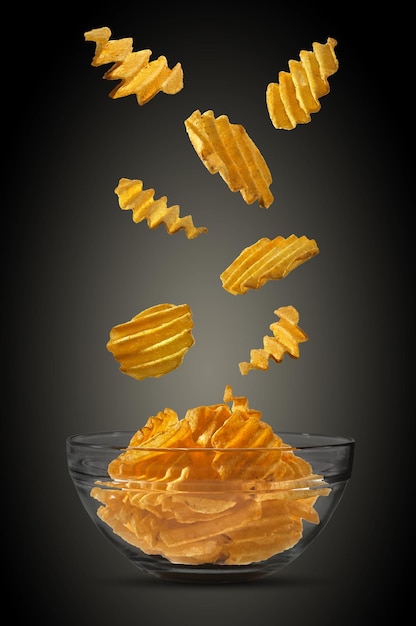 Gerillte Kartoffelchips, die in einer Glasschüssel vor einem schwarzen Hintergrund mit Kopierbereich für Textbilder herunterfallen Knusprige Chips Werbung Closeup