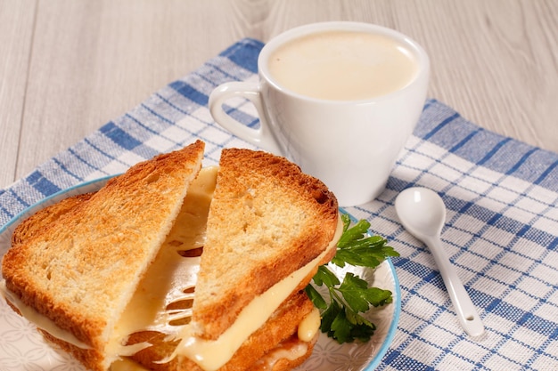 Geröstete Brotscheiben mit Käse und grüner Petersilie auf weißem Teller, Tasse Kaffee und Löffel mit blauer Küchenserviette. Gutes Essen zum Frühstück.