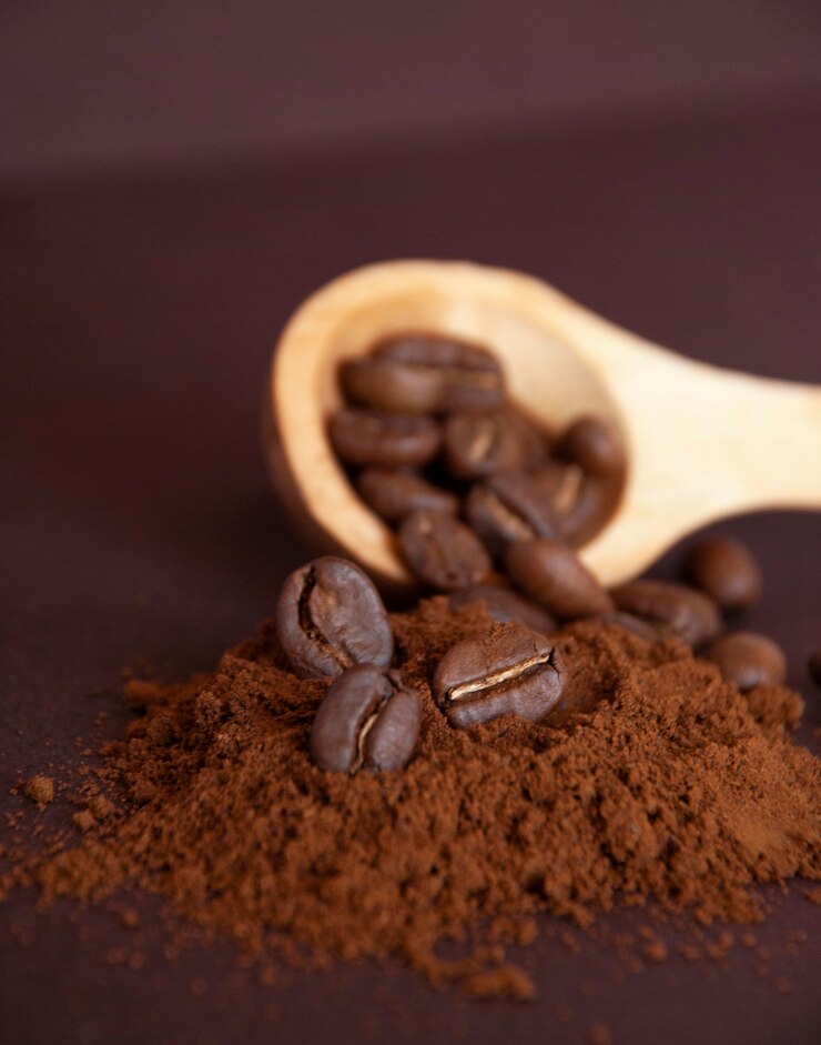 Geröstete Kaffeebohnen auf gemahlenem Kaffee und in einem Holzlöffel.
